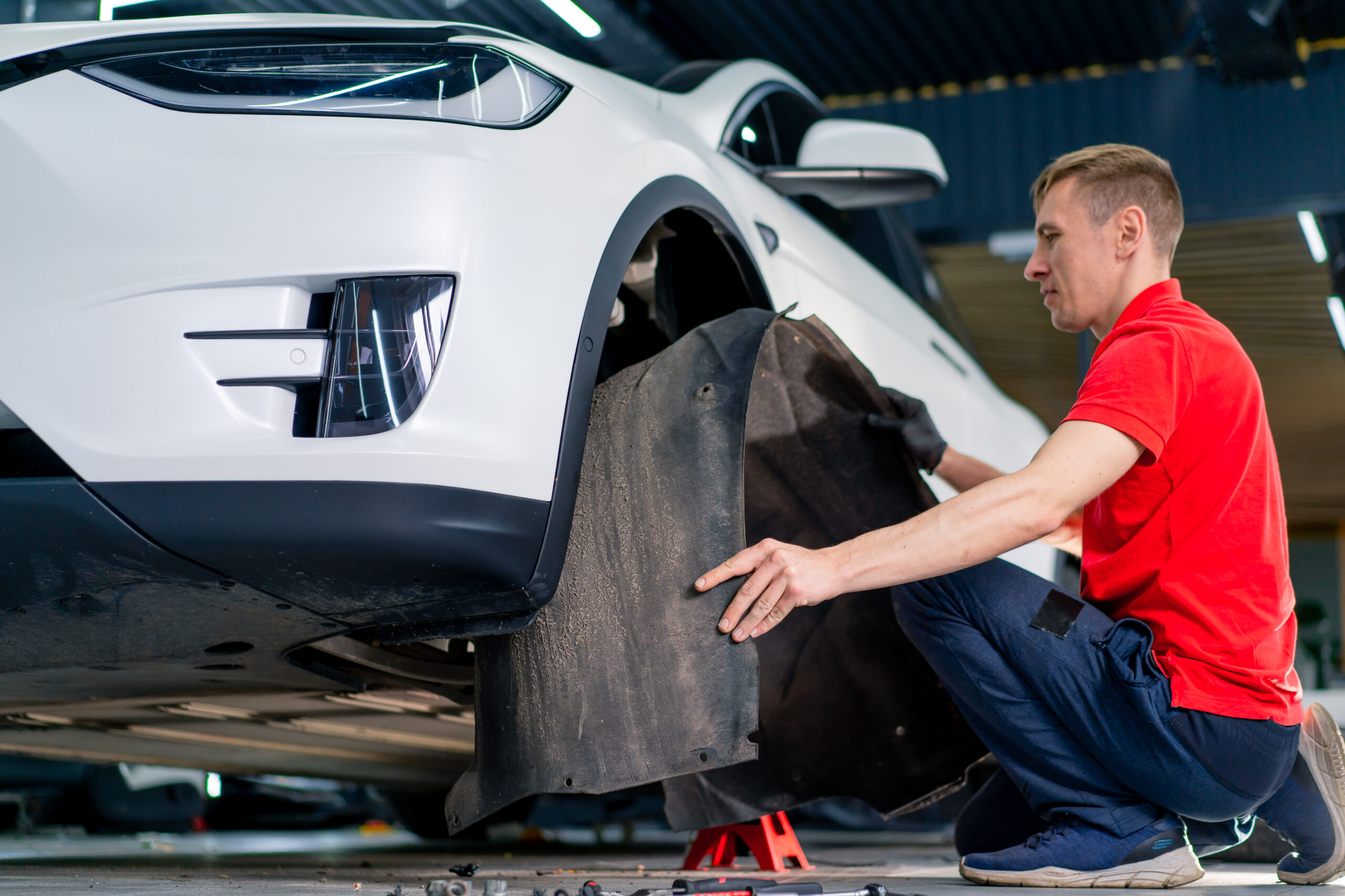 A car service worker removes fender liner of white luxury car while washing and dry cleaning auto detailing